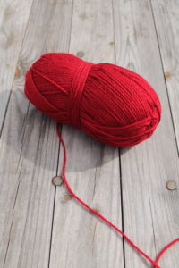Rotes Wollknäul mit rotem abgehenden Faden